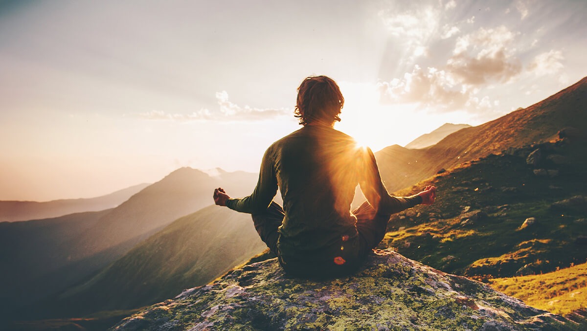Mann meditiert auf Berggipfel im Sonnenaufgang