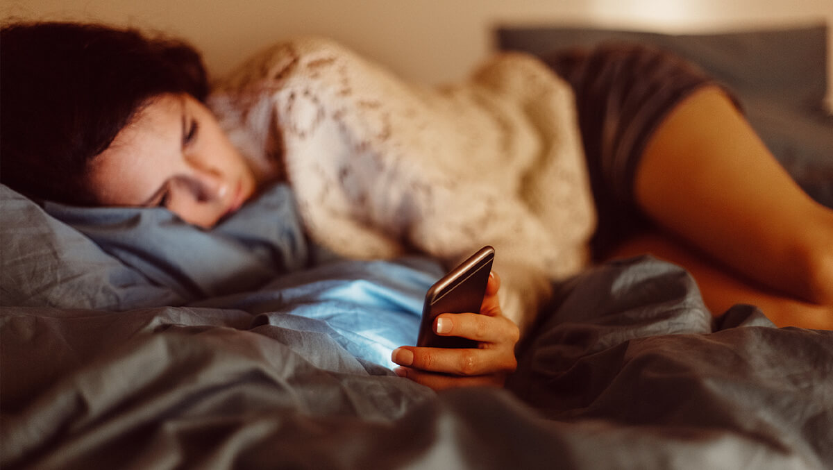 Frau liegt mit Handy im Bett