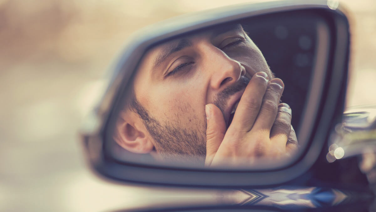 Übermüdet Autofahren: Mann gähnt in Autospiegel