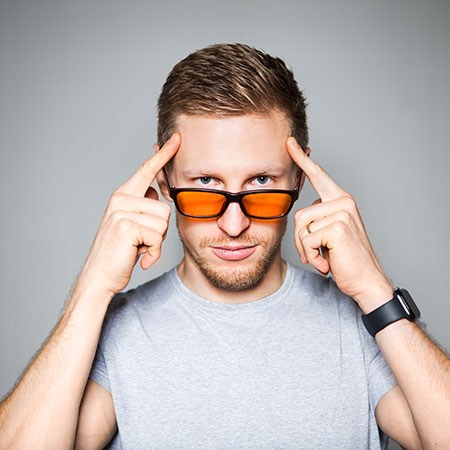 Portrait von Nico Airone mit orangener Brille und Fingern an Schläfen