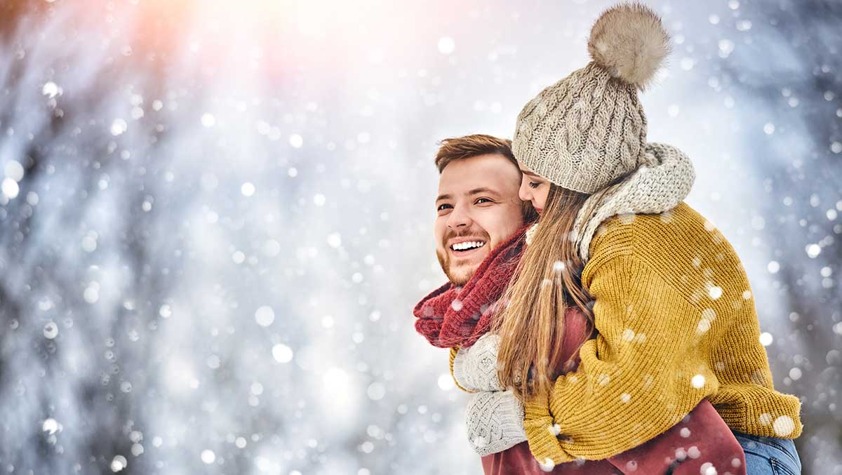 Mann trägt Frau Huckepack im Schnee