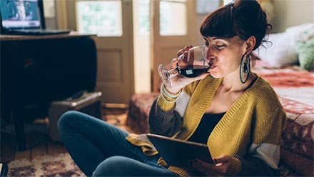 Junge Frau trinkt Wein auf dem Boden sitzend mit Tablet in der Hand