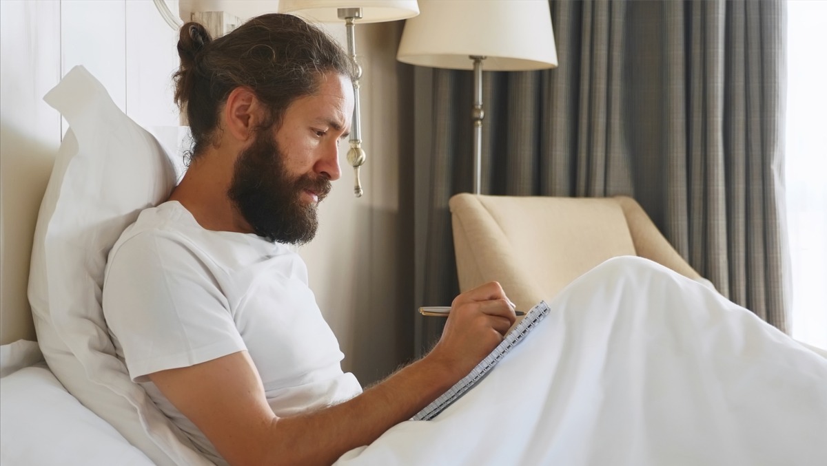 Mann schreibt im Bett sitzend in sein Schlaftagebuch