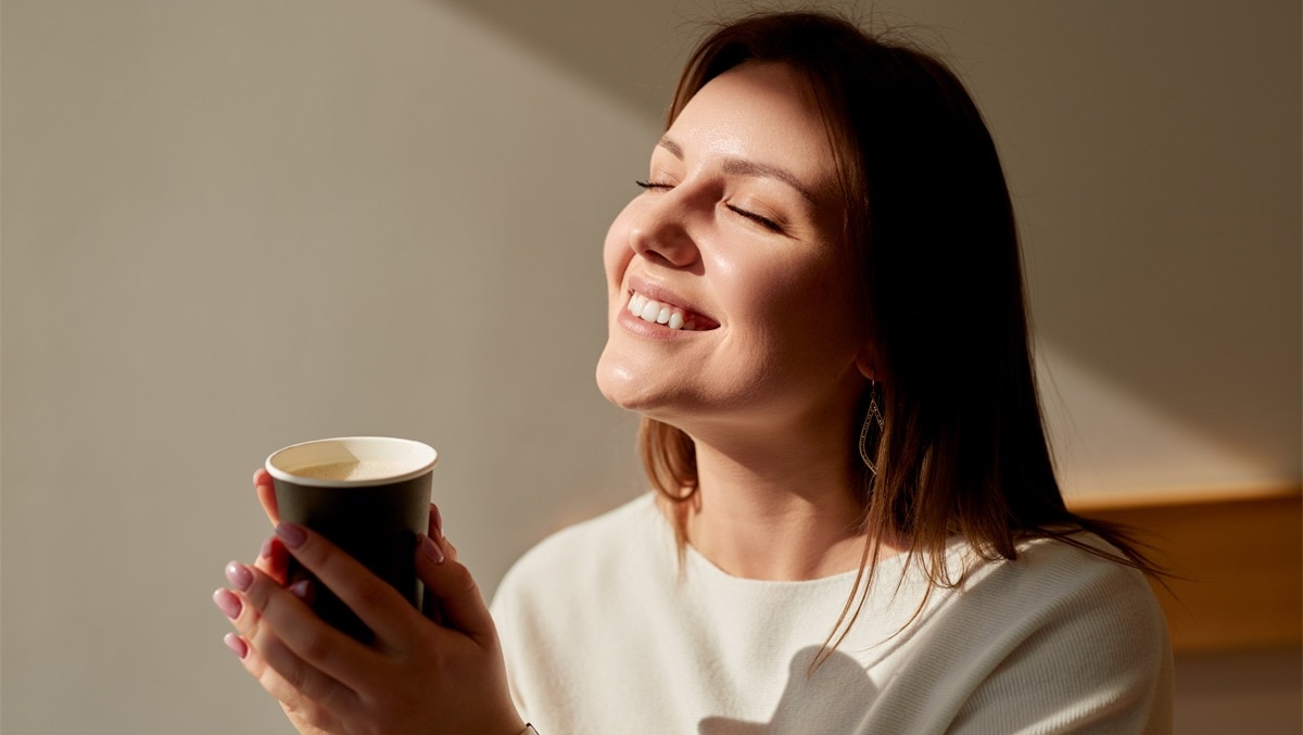 Frau genißet ein Heißgetränk am Morgen und lässt sich die Sonne ins Gesicht scheinen