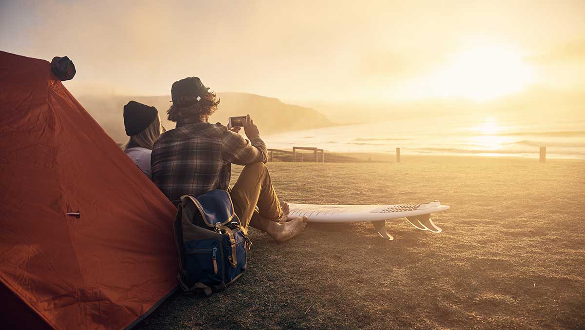 Paar sitzt vor Zelt am Strand bei Sonnenuntergang