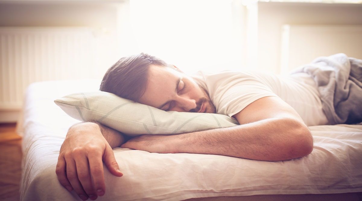 Ein Mann liegt in Buachlage schlafend auf dem Bett und hat Arm unter dem Kissen